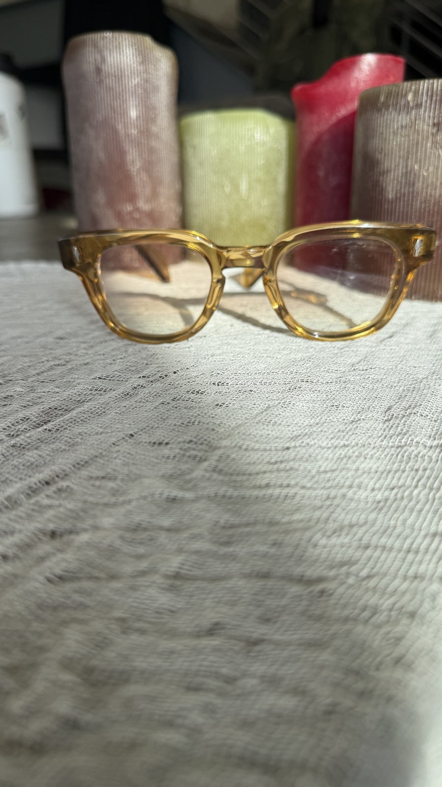 Frame Style 1 in wheat acetate, resting on linen with candlelight behind