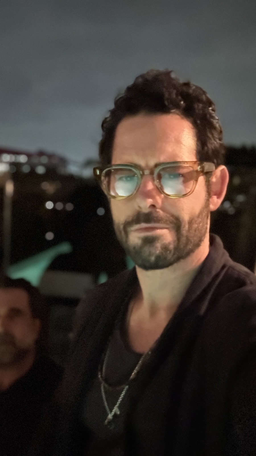 A man wearing wheat acetate Moonshades at night, city lights behind him